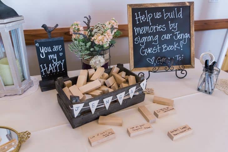 Jenga wooden blocks with wedding guest signatures and a sign that says, "Help us build memories by signing our Jenga Guest Book!"